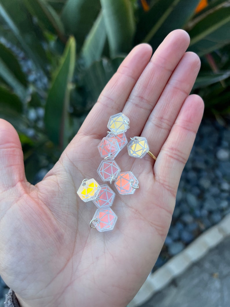 May include: A hand holding a group of iridescent, clear plastic, geometric shapes with silver rings. The shapes are reminiscent of dice.