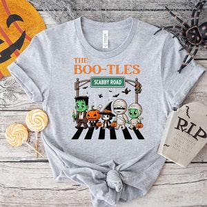 May include: A gray t-shirt with a graphic of a crosswalk with five cartoon characters dressed as Halloween monsters. The text "The Boo-Tles" and "Scabby Road" are on the sign above the crosswalk.