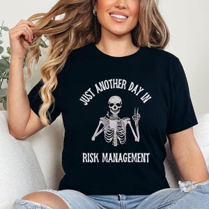 May include: Black t-shirt with a white skeleton graphic and the text "Just another day in risk management".