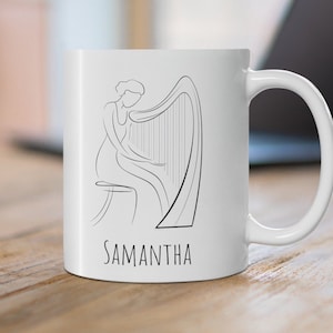 May include: White ceramic mug with a black line drawing of a person playing a harp. The mug has the name "SAMANTHA" printed on the bottom.