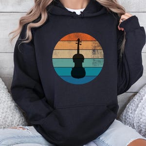 May include: Black hoodie featuring a vintage-style graphic of a violin silhouette against a sunset backdrop. The graphic has a distressed look with orange, yellow, blue, and green colours.