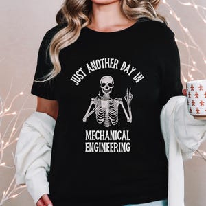 May include: Black t-shirt with a white skeleton holding a coffee cup and giving a peace sign. The text "Just another day in Mechanical Engineering" is printed on the shirt.