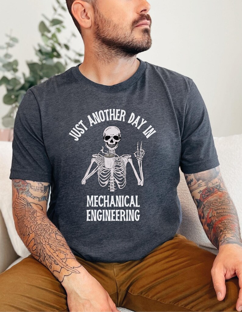 May include: A dark gray t-shirt with a white skeleton holding a coffee cup and the text "Just another day in mechanical engineering".