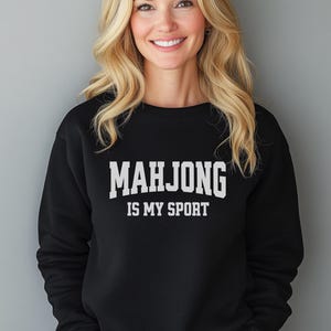 May include: Black crew neck sweatshirt featuring the white text "MAHJONG IS MY SPORT". The sweatshirt is made of a soft material. The design is a casual, game-themed apparel item, suitable for everyday wear.