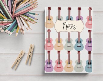 May include: A white notebook with a colorful guitar pattern and the word "Notes" in a brown frame. The notebook is surrounded by colored pencils and wooden clothespins.