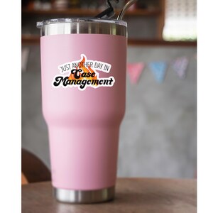May include: Pink stainless steel travel mug with a white sticker that says "Just another day in Case Management" with a flame graphic.