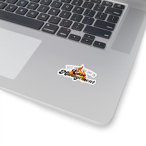 May include: A white sticker with a black and orange flame design. The text "Just another day in Case Management" is written in black on the sticker.