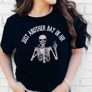 May include: Black t-shirt with a white skeleton graphic holding a coffee cup and the text "Just another day in HR".