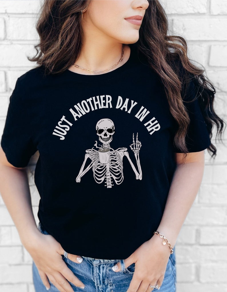 May include: Black t-shirt with a white skeleton graphic holding a coffee cup and the text "Just another day in HR".