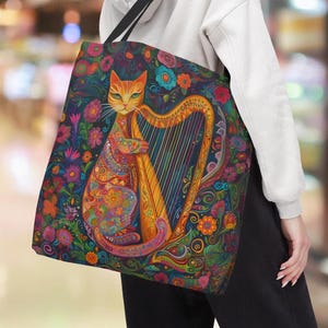 May include: A colorful tote bag with a cat playing a harp. The cat is orange and white with a detailed design of flowers and swirls. The harp is gold and has a rainbow design.