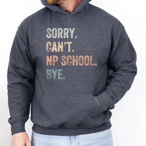 May include: A dark heather grey hoodie with a vintage-style graphic that reads "Sorry. Can't. NP School. Bye."