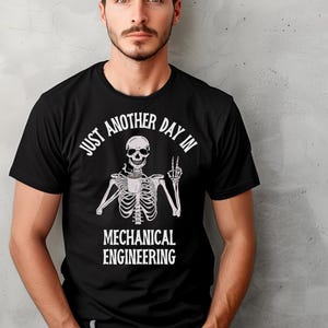 Pode incluir: Camiseta preta com um esqueleto branco segurando uma xícara de café e fazendo um sinal de paz. O texto na camiseta diz "Just another day in Mechanical Engineering."