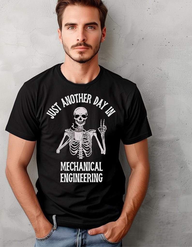 May include: Black t-shirt with a white skeleton holding a coffee cup and making a peace sign. The text on the shirt reads "Just another day in Mechanical Engineering."