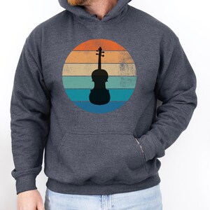 May include: Dark gray hoodie with a front pocket. The design features a black violin silhouette inside a circle with horizontal stripes in orange, teal, and blue, evoking a retro sunset.