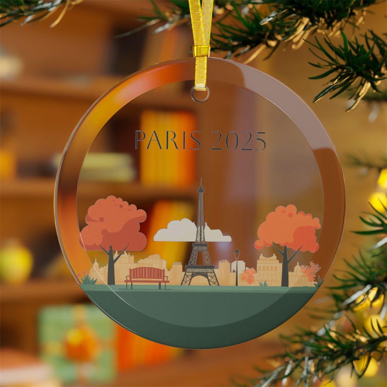 May include: A clear glass ornament with a gold ribbon and a printed image of the Eiffel Tower, trees, and the text "PARIS 2025".