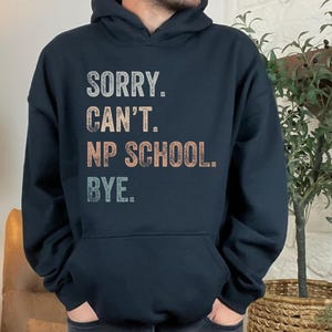 May include: A black hoodie with a vintage-style graphic that reads "SORRY. CAN'T. NP SCHOOL. BYE."