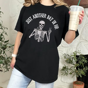 May include: Black t-shirt with a skeleton holding a coffee cup and the text "Just another day in HR".