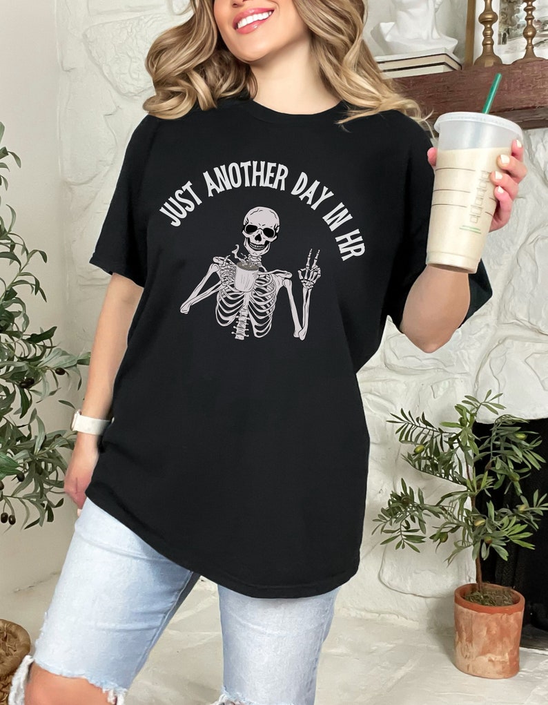 May include: Black t-shirt with a skeleton holding a coffee cup and the text "Just another day in HR".