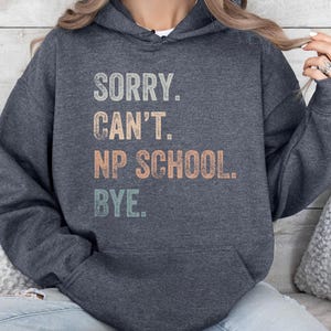 May include: A dark gray hooded sweatshirt with the text "SORRY. CAN'T. NP SCHOOL. BYE." printed in a vintage style with colorful lettering.