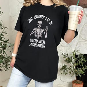 May include: Black t-shirt with a skeleton holding a coffee cup and the text "Just another day in mechanical engineering".