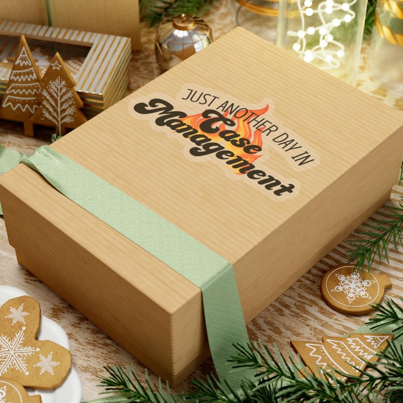 May include: A brown gift box with a green ribbon. The box has a sticker on it that says "Just Another Day in Case Management" with a flame design.