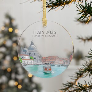 May include: A clear, round ornament with a gold ribbon. The ornament features a colorful illustration of a Venetian canal scene with the text "ITALY 2026 CUSTOM MESSAGE". The scene includes buildings, water, and a boat.