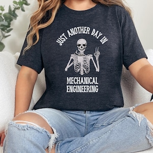 May include: A dark gray t-shirt with a white skeleton graphic and the text "Just another day in mechanical engineering".