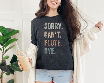 Może przedstawiać: Szary t-shirt z nadrukiem "SORRY. CAN'T. FLUTE. BYE." w stylu vintage. Tekst jest w odcieniach różowego, niebieskiego i żółtego.