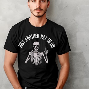 May include: Black t-shirt with a white skeleton holding a coffee cup and making a peace sign. The text "Just another day in HR" is written in a circle around the skeleton.