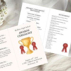 Puede incluir: Un programa de ceremonia de premios de color crema, diseño plegado en tres, con una ilustración de trofeo dorado con cintas rojas. El programa incluye detalles del evento, homenajeados y la fecha: 18 de agosto de 2027, 18:00, Alfred Auditorium, Princeton, NJ.