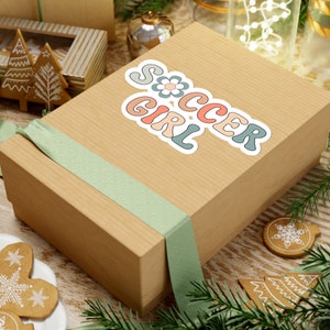 May include: A brown gift box with a green ribbon and a sticker that says "Soccer Girl" in colorful letters with a flower design.