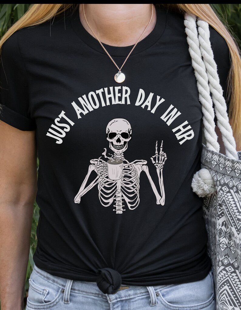 May include: Black t-shirt with a white graphic of a skeleton holding a coffee cup and the text "Just another day in HR".