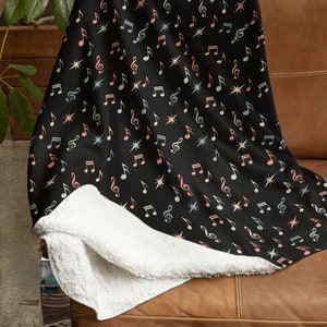 May include: A black fleece blanket with a colorful music note and star pattern. The blanket is folded and draped over a brown leather couch.