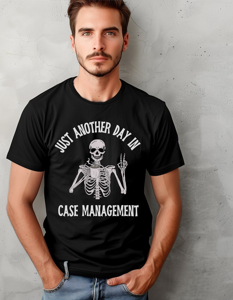 May include: Black t-shirt with a white graphic of a skeleton holding a coffee cup and giving the peace sign. The text reads "Just another day in case management."