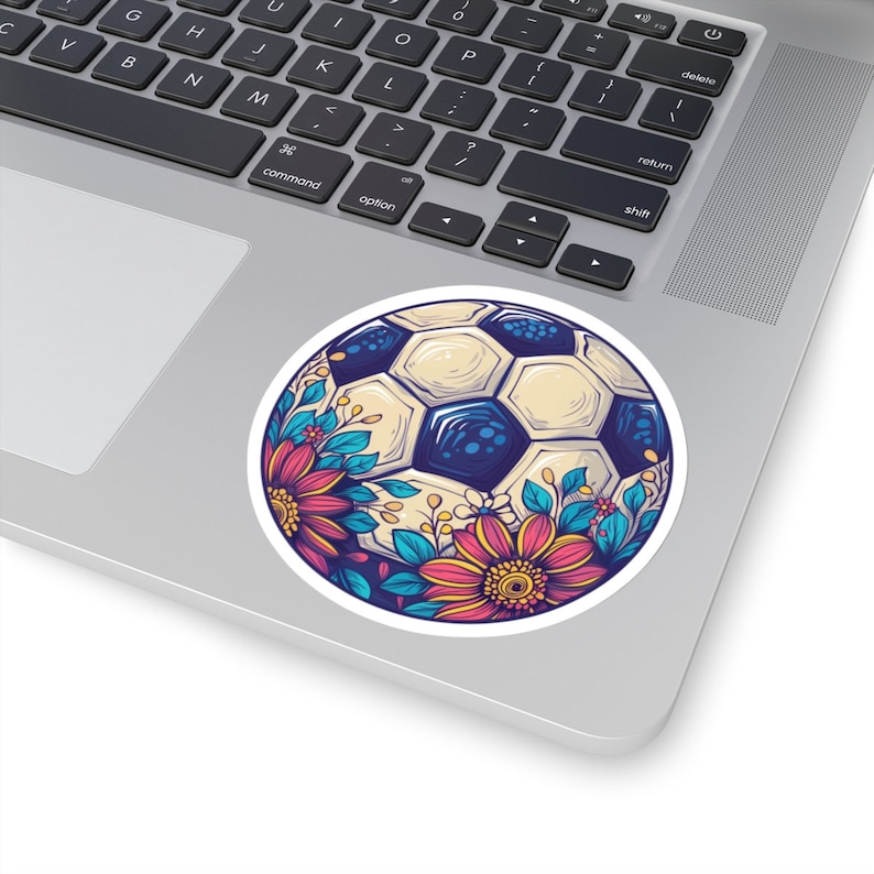 Puede incluir: Un bal&oacute;n de f&uacute;tbol blanco con detalles azules y negros rodeado de flores coloridas. Las flores son rosas, rojas, azules y amarillas.