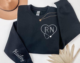 May include: Black sweatshirt with a white heart design featuring the letters "RN" and a stethoscope. The sleeve has the name "Hailey" written in white.
