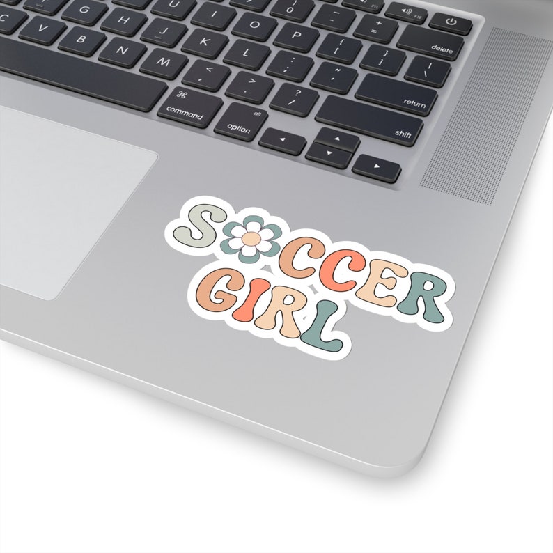 May include: A sticker with the words "Soccer Girl" in a retro font with a flower in the "S". The letters are in shades of pink, orange, blue, and green.