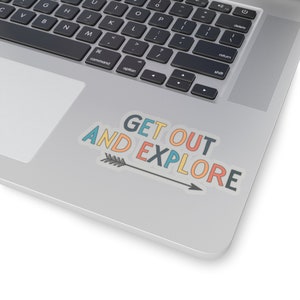 Può includere: Un adesivo con le parole "GET OUT AND EXPLORE" in verde acqua, arancione e giallo, con una freccia nera che punta verso destra. L'adesivo è su un laptop argentato.
