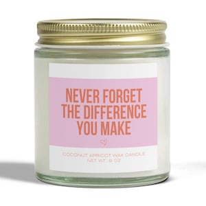 May include: A glass jar candle with a pink and orange label that reads "NEVER FORGET THE DIFFERENCE YOU MAKE". The candle is a coconut apricot scent and weighs 9 ounces.
