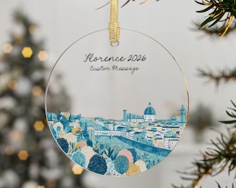 May include: A circular clear acrylic ornament featuring a printed illustration of the Florence skyline in shades of blue, yellow, and pink. The text Florence 2026 and Custom Message is printed in black. It hangs from a gold ribbon loop.