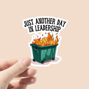 Può includere: Un adesivo con un cassonetto verde in fiamme e il testo "Just another day in leadership."