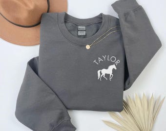 May include: A dark gray sweatshirt with a white horse and the name "TAYLOR" embroidered on the front.
