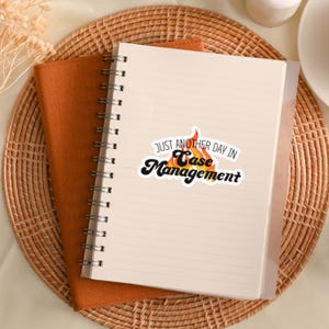 May include: A white notebook with a spiral binding and a sticker that says "Just another day in Case Management". The sticker has a flame design with orange and yellow colors.