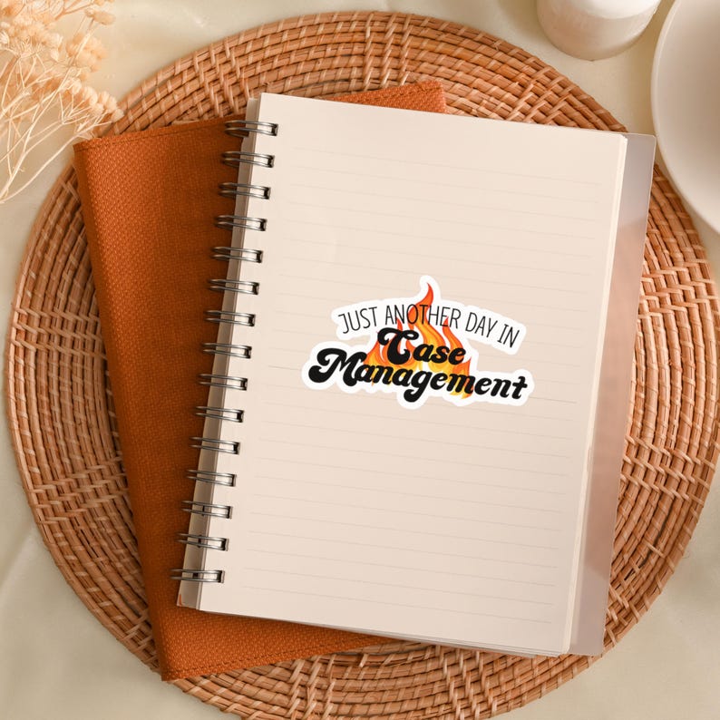 May include: A white notebook with a spiral binding and a sticker that says "Just another day in Case Management". The sticker has a flame design with orange and yellow colors.
