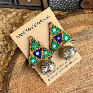 May include: A pair of green, blue, and gold triangle earrings with silver bell charms. The earrings are handmade and have a bohemian style. The earrings are on a brown card with the text "HANDMADEAHOLIC @handmadeaholic_by_mishka www.handmadeaholicmishka.com"