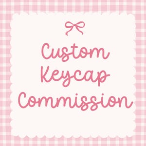 May include: A square sign with a scalloped edge featuring a pink and white gingham background. The text Custom Keycap Commission is written in a pink cursive font, centered below a small pink bow icon at the top of the white central area.