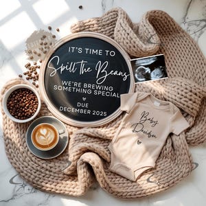 Pode incluir: Um anúncio de gravidez com um quadro-negro que diz "It's Time to Spill the Beans", um body de bebê, uma ultrassonografia, grãos de café e um café com leite. O anúncio está em um cobertor de malha bege.