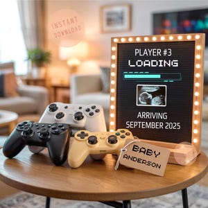 Può includere: Un tavolo di legno mostra quattro controller per videogiochi neri, bianchi e gialli. Un cartello incorniciato con luci recita "Player #3 Loading" con un'immagine ecografica e "Arriving September 2025." Un'etichetta dice "Baby Anderson."