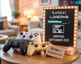 Op de afbeelding: Een houten tafel toont vier gamecontrollers in zwart, wit en geel. Een omlijst bord met lampjes leest "Player #3 Loading" met een echografie en "Arriving September 2025." Een label zegt "Baby Anderson."