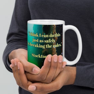 May include: White ceramic mug with a blue and green abstract design. The mug features a quote in yellow text: "I think I can do this just as safely by breaking the rules." - Stockton Rush.